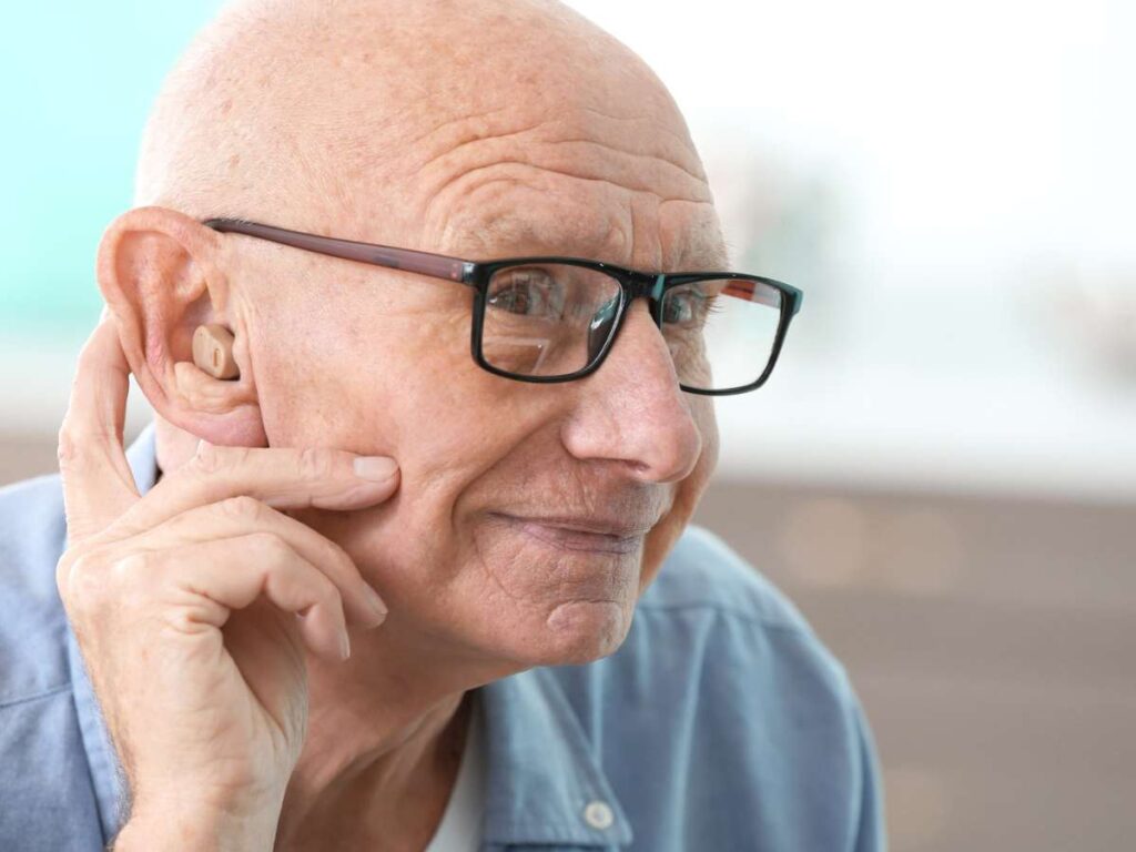 old man touching hearing aid in ear