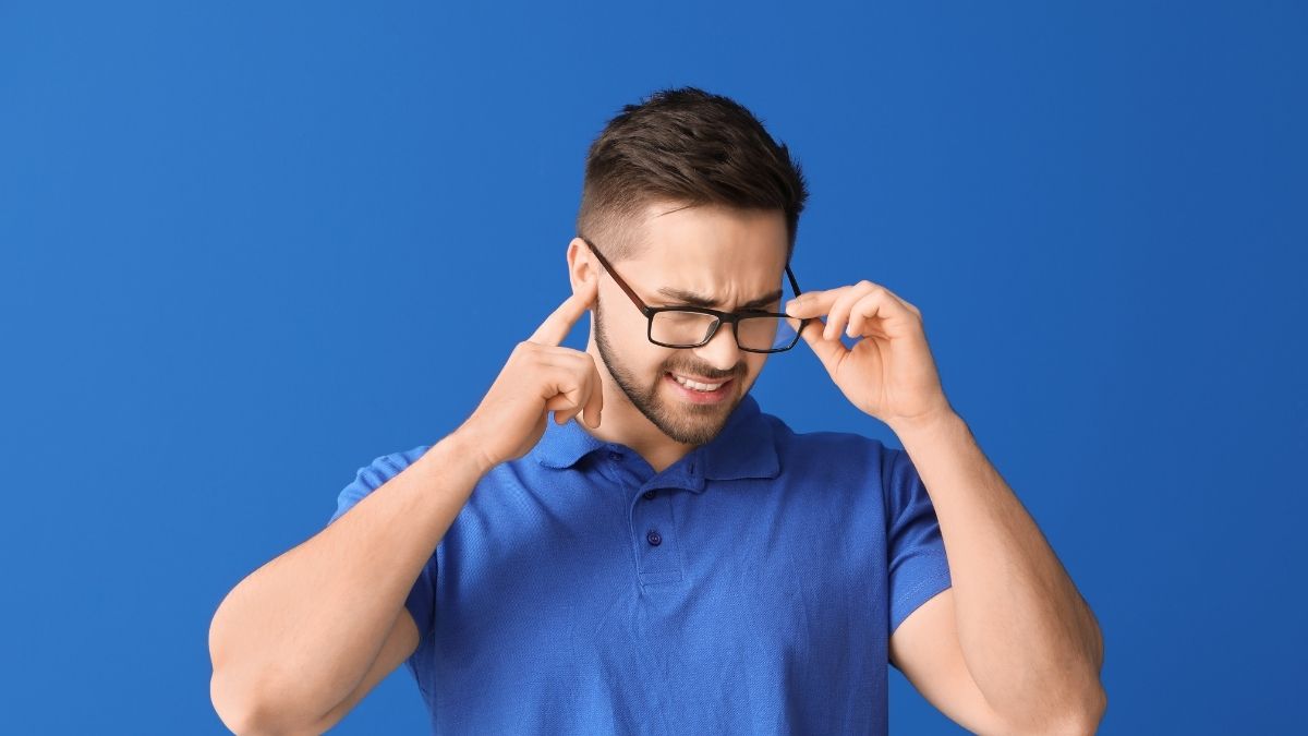 Man in a blue shirt with pain in his ears from tinnitus.