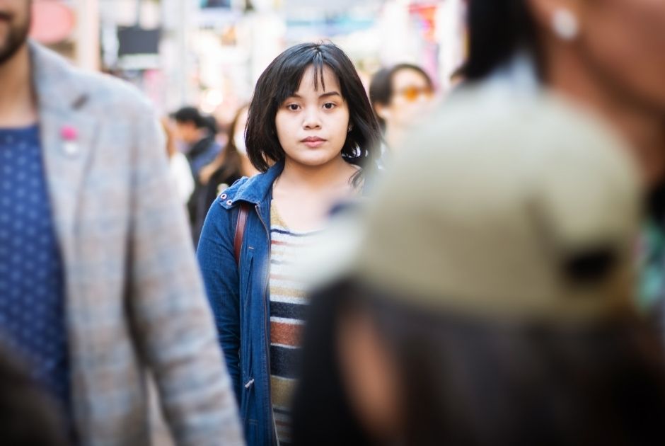 Young asian lady wearing a blue jacket staring forward in a crowded area.