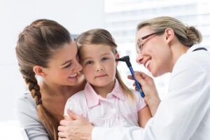 Young girl with a doctor examining her ear while her mother comforts her.