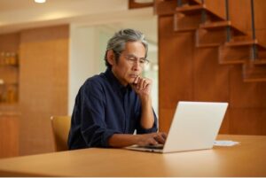 Middle aged asian man on a laptop looking for an audiologist on the gold coast